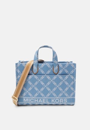 Niebieska torba typu tote marki Michael Kors z białym wzorem łańcucha, dwoma górnymi uchwytami oraz regulowanym beżowym paskiem na ramię na jednolitym tle.