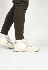Witte en mintgroene sneakers met een bovenwerk van suede en mesh, met een gestructureerde zool en minimalistisch design; gedragen met donkere joggingbroeken.
