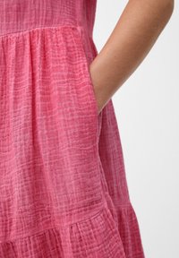 Robe en coton rose, texturée, avec un design à volants et des poches latérales, dotée d'une finition douce et froissée ainsi que d'un subtil détail tissé.