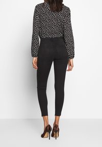 Jeans skinny de tiro alto negros combinados con una blusa de lunares en blanco y negro, con mangas largas abullonadas y una textura sutil.