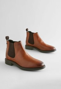 Botas Chelsea de cuero marrón con paneles laterales elásticos, superficie texturizada, tirador y una suela de goma baja y plana.