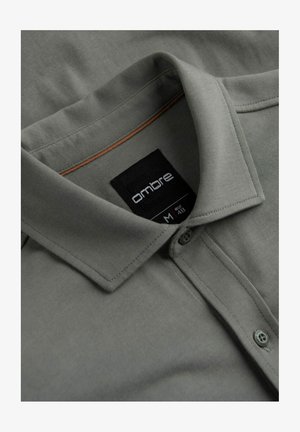 Gray polo shirt with a collar, two buttons, and a brown accent at the neckline. Label visible with brand and size information. Soft fabric texture.