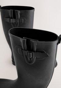 Sorte gummiknæhøje støvler med justerbare stropper, glat tekstur og runde toppe. Designet til holdbarhed og vandtæt brug.