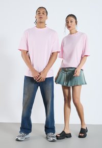 To modeller har på seg uformelle antrekk. Den mannlige modellen har på seg en lyserosa oversized t-skjorte og mørkeblå jeans. Den kvinnelige modellen har på seg en rosa t-skjorte og et denimskjørt.