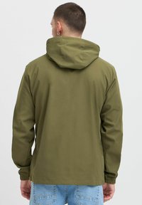 Jachetă cu capuz de culoare verde măslin, confecționată dintr-un material neted, cu manșete elastice și un design simplu, văzută din spate.