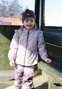 Lila gestepptes Jacke mit Blumenmuster, passende Hose und dunkelviolette Mütze. Auffällige Details sind die Rüschenärmel und hölzerne Akzente.