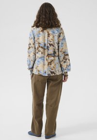 Hosszú ujjú ing kék, bézs és barna batikolt mintával, hátul hasítékkal és laza szabással, laza khaki nadrággal párosítva.