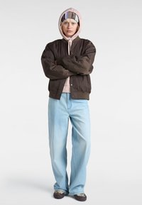 Brun quiltet bomberjakke over en lys pink hoodie, sammen med lyseblå vide jeans og mønstrede sneakers.