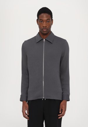 Giacca grigia con chiusura a zip, colletto a polo, texture a coste e maniche lunghe. Presenta una zip argentata e un design minimalista.