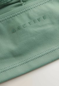 Grønne stof med en glat tekstur har prægede "ACTIVE"-mærkning. Synede kanter og en subtil glans forbedrer designet.
