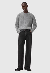 Maglione grigio fluffy a maglia, jeans neri a vestibilità ampia, cintura nera. Il maglione ha un collo rotondo; le scarpe presentano un accentuato contrasto sulla punta.