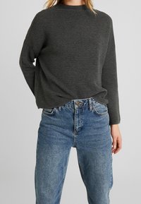 Grauer Rippstrickpullover mit hohem Kragen und langen Ärmeln, kombiniert mit blauen hochtaillierten Jeans in einem lässigen Schnitt.