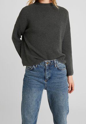 Maglione grigio a costine con collo alto e maniche lunghe, abbinato a jeans blu a vita alta, in un fit casual.