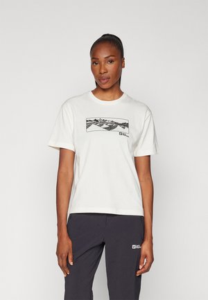 White cotton t-shirt featuring a black mountain graphic across the chest. Short sleeves and a round neckline. Paired with dark pants.