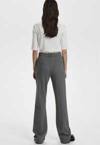Pantaloni larghi grigi chiari realizzati in tessuto morbido, con vita modello con cintura e due tasche posteriori. Texture liscia, design su misura.