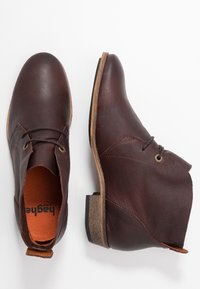 Stivaletti in pelle marrone con finitura testurizzata, design con lacci, apertura laterale e tacco basso impilato. L'interno presenta una soletta arancione.