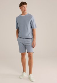 Světle modrý pletený svetr s krátkým rukávem spárovaný se světle modrými šortkami a bílými teniskami. Tento outfit má jednoduchý a neformální design.