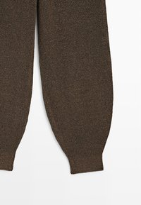 Bruin gebreide stof met een close-up van twee mouwen die een gedetailleerde textuur en geribbelde manchetten tonen op een witte achtergrond.