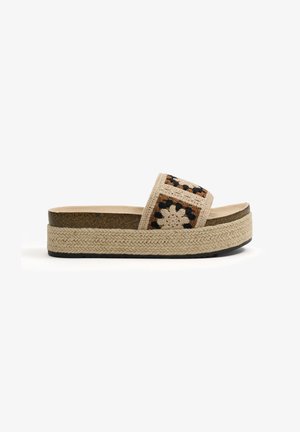 Sandalia de plataforma con suela beige tejida y tiras de ganchillo con un diseño de cuadros en marrón, crema y negro.
