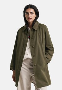 Abrigo verde oliva con cierre de botón, cuello extendido y mangas largas. Presenta un corte holgado y está hecho de una tela suave y duradera.
