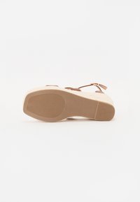 Sandale marron à lanières avec une semelle de type espadrille tissée, présentant un fond en caoutchouc texturé et une bride de cheville réglable pour un maintien sûr.