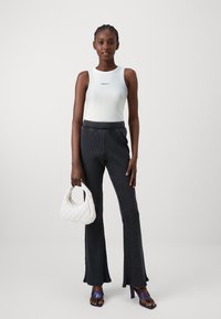 Bílý ribbed top s potiskem, černé zvonové kalhoty s vertikálními pruhy a bílá prošívaná kabelka. Modelka má na sobě fialové sandály na podpatku.