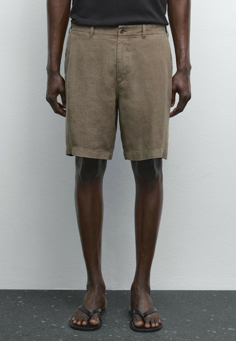 Linnebyxor i en dämpad brun färg, med rak passform, framknappning och sidofickor. Bärs med svarta flip-flops.