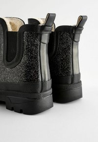 Bottines noires avec un design à paillettes éparses, finition mate en caoutchouc, panneaux latéraux en tissu et languettes à l'arrière. Semelle texturée.