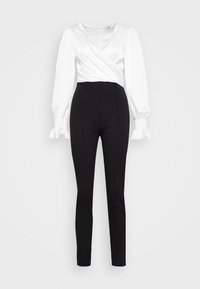 Vit satinblus med lång ärm och smockade manschetter, tillsammans med svarta, figurnära byxor. Släta texturer genom hela plagget.