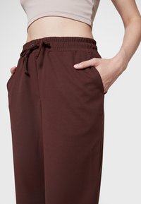 Bruna, lätta, elastiska byxor med midjeband, sidofickor och en mjuk textur. Designade för komfort och rörelsefrihet.