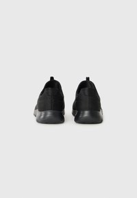 Des baskets noires de sport avec une tige en mesh texturé, un talon arrondi et une semelle en caoutchouc. Comprend une languette au dos pour un enfilage facile.