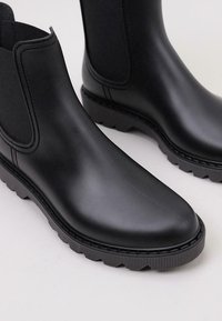 Botas de tobillo de goma negras con paneles laterales elásticos, suela texturizada y un acabado liso con un diseño de puntera redonda.
