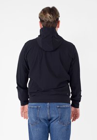 Giubbotto leggero nero con cappuccio, polsini e orlo elasticizzati. Abbinato a jeans blu con tasche posteriori standard.