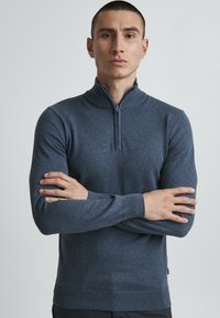 Maglione blu scuro con zip al collo, maniche lunghe, polsini e orlo a costine. Realizzato in un tessuto liscio e texturizzato. Design semplice e pulito.