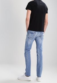 Czarna krótka koszulka z krótkim rękawem w połączeniu z jasnoniebieskimi dżinsami slim-fit, z poszarpanymi detalami i białymi sneakersami. Widok z tyłu.