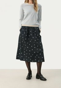 Pull rayé bleu clair et beige associé à une jupe midi noire ornée de motifs floraux blancs. L'ensemble est complété par des mocassins noirs et des collants.