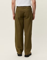 Ελαιόλαδο πράσινα παντελόνια με φαρδιά πόδια από υφασμάτινη υφή, με δύο πίσω τσέπες και μέση μεσαίου ύψους, συνδυασμένα με μαύρα υποδήματα.