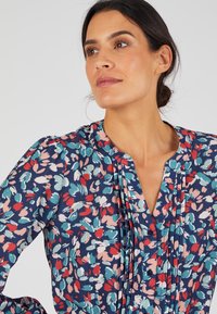 Blusa floreale in blu navy con motivi astratti colorati in rosa, rosso e turchese. Presenta pince e una scollatura a V con bottoni.
