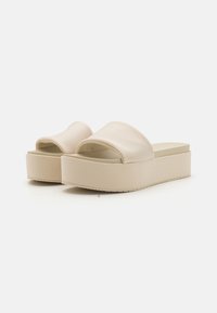 Beige platform slide sandals with a smooth, rounded strap design and a textured sole. Material appears synthetic with a matte finish.