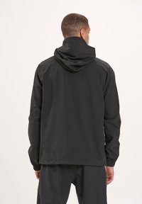 Sort hættejakke lavet af glat, let materiale med elastiske manchetter og en løs pasform. Har et enkelt design uden synlige logoer.