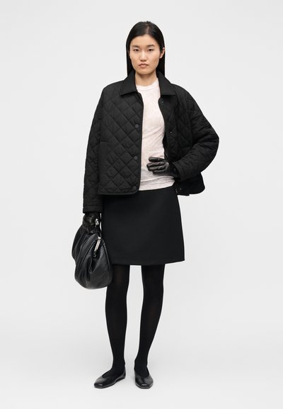 Μαύρο μπουφάν με καπιτονέ σχέδιο, ανοιχτόχρωμο τοπ, μαύρη φούστα, μαύρες καλτσοδέτες και γάντια. Το μοντέλο κρατά μια μεγάλη μαύρη τσάντα. Απλή, λιτή σιλουέτα.