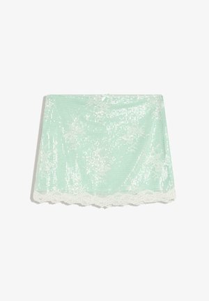 Lichtgroene mini-rok met witte bloemenkantlaag, pailletten, geschulpte kanten zoom en een klein strikje in het midden van de tailleband.