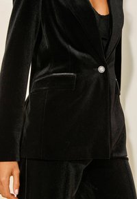 Must must-särk, millel on vormitud disain, ühe kristall-nööbiga kinni pandav ja külgtasku. Sujuv tekstuur ja elegantne viimistlus.