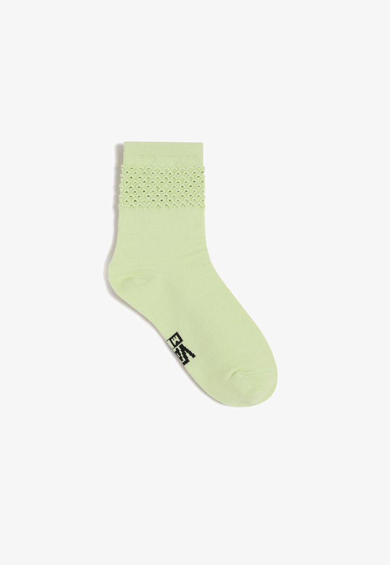 Hellgrüne Knöchelsocken mit einem strukturierten, spitzenähnlichen Design am oberen Rand, aus einem glatten, weichen Stoff und mit einem schwarzen Logo an der Sohle.
