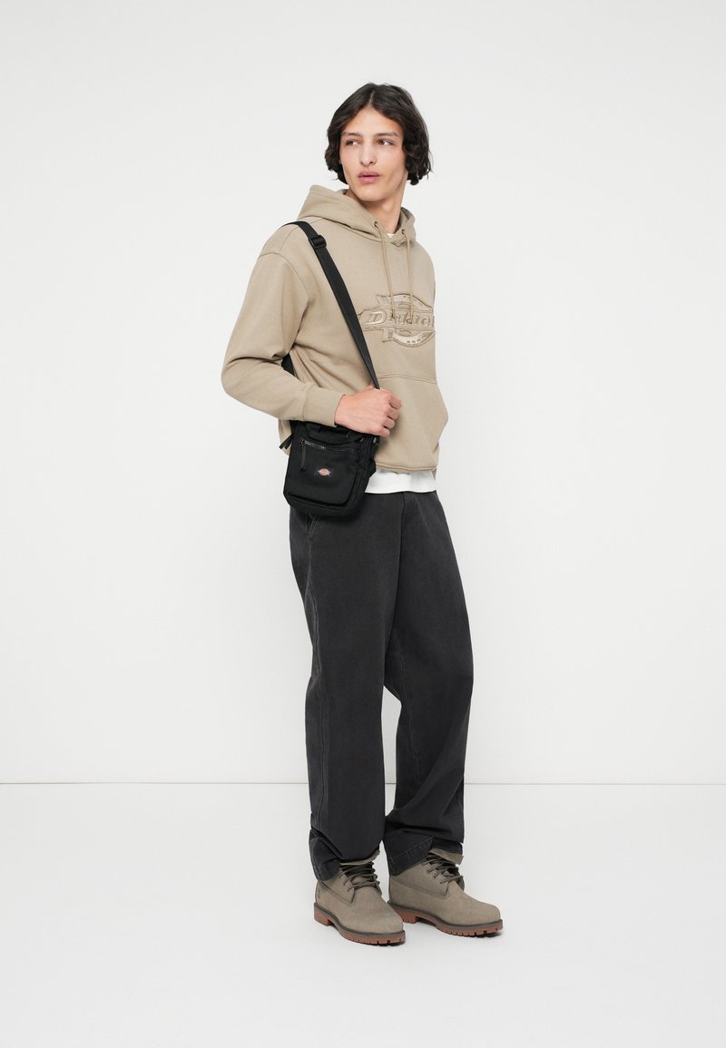 Beige hoodie with a logo, gray loose pants, black crossbody bag, and gray boots with brown soles; minimal design, smooth texture.