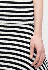 Ύφασμα με ρίγες σε ασπρόμαυρο, ραβδωτό, με οριζόντιες ρίγες, υφασμένη επιφάνεια. Ένα χέρι ακουμπά στο υφασμένο ύφασμα στην περιοχή της μέσης.