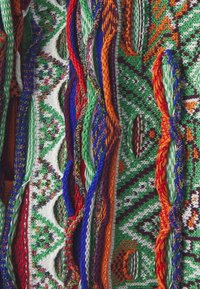 Tissu coloré présentant des motifs complexes en vert, rouge, bleu et orange. Le matériau est tissé, mettant en avant des nœuds et des boucles détaillés.