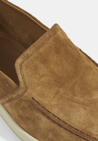 Braunes Wildleder-Slipper mit glatter Textur, der eine gestickte Akzentuierung und ein abgerundetes, flaches Design aufweist.