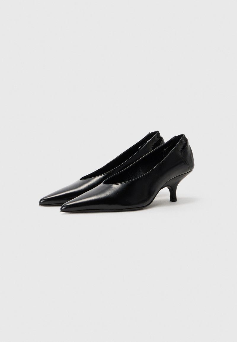Schwarze Leder Schuhe mit spitzer Zehenpartie, niedrigem Kitten-Absatz und ausgeschnittenen Seiten, die eine glatte Textur und ein minimalistisches Design aufweisen.