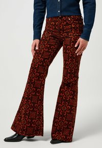 Uppblåsta byxor i rödbrunt tyg med ett abstrakt geometriskt mönster. Har hög midja, subtila fickor och en mjuk textur.